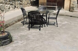 Un patio al aire libre con una mesa redonda y cuatro sillas, una planta en maceta y un muro de piedra.