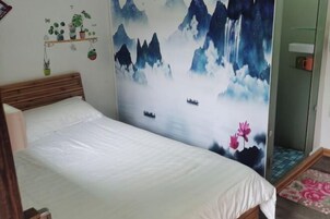 Un dormitorio con una cama, un mural en la pared de montañas y agua, y un estante pequeño con plantas.