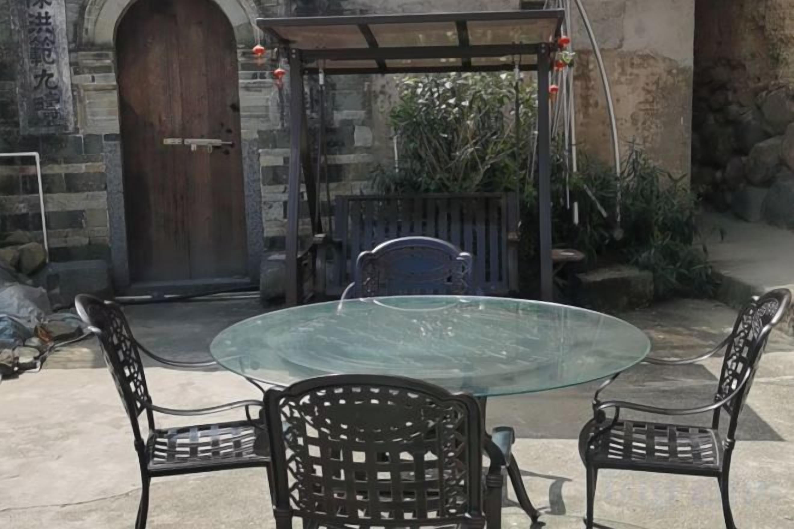 A glass-top table with four chairs, a wooden door, and a stone wall.