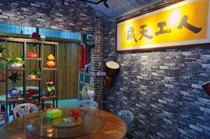 Una habitación con pared de ladrillo, puerta de madera, mesa redonda de vidrio y una estantería con plantas y objetos decorativos.