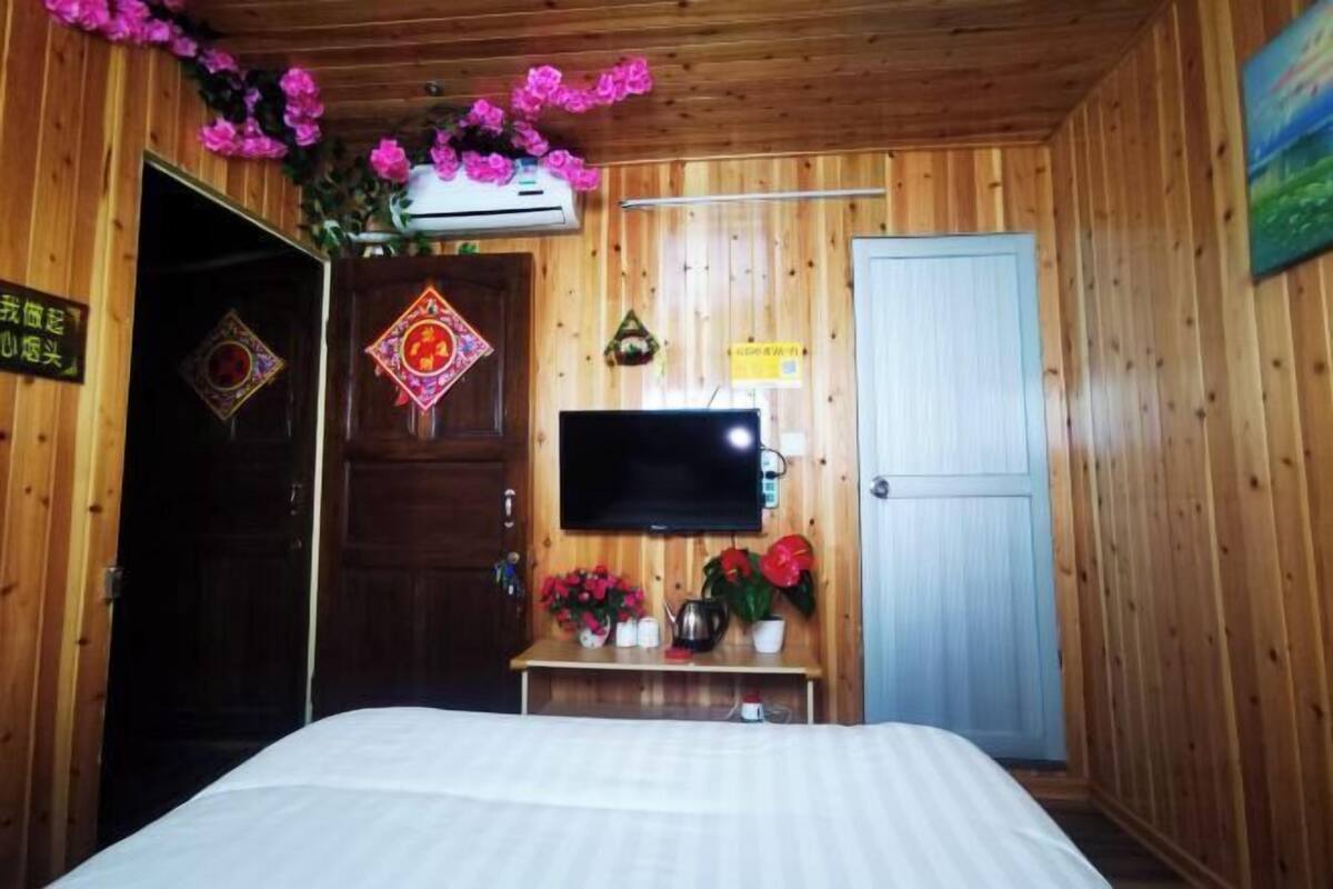 Ein Zimmer aus Holz mit einem Bett, einem Fernseher und einem kleinen Tisch mit Blumen.
