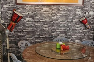 Una habitación con pared de ladrillo, una mesa redonda de vidrio y dos tambores rojo y negro.