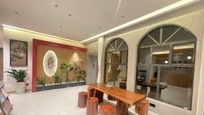 Um hall com mesa e banquetas de madeira, plantas em vasos e uma grande janela em arco.