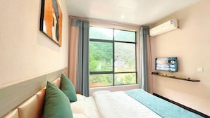 Quarto de hotel com uma cama, uma televisão sobre um suporte, uma janela com cortinas e um aparelho de ar condicionado na parede.