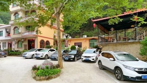 Uma área de estacionamento com vários carros, um edifício com telhado vermelho e uma árvore ao primeiro plano.