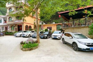 A parking area with multiple cars, a building with a red roof, and a tree in the foreground. - Yishan Bishui Inn (Libo)