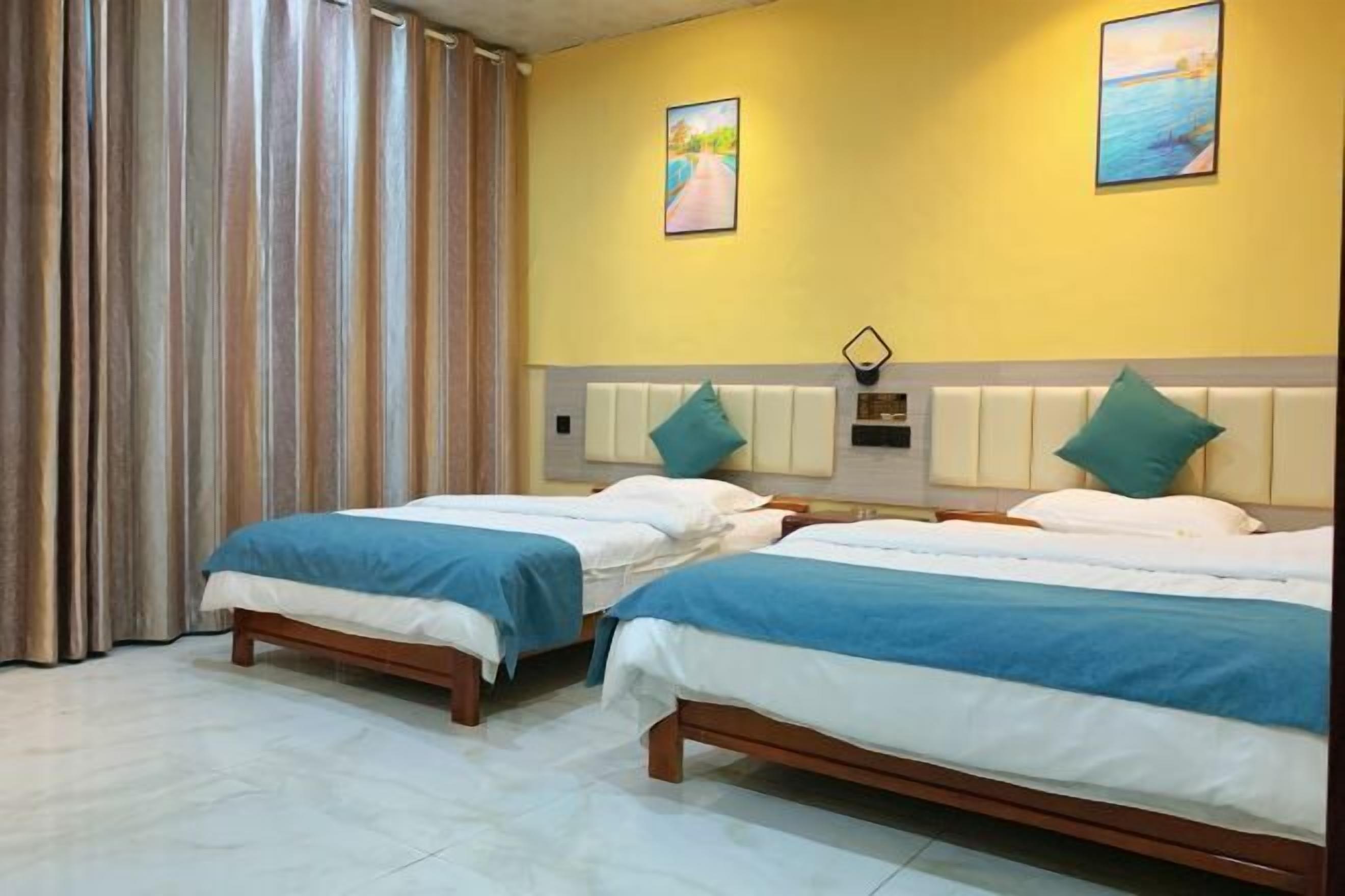 Una habitación de hotel con dos camas, un ventanal con cortinas y dos cuadros en la pared.