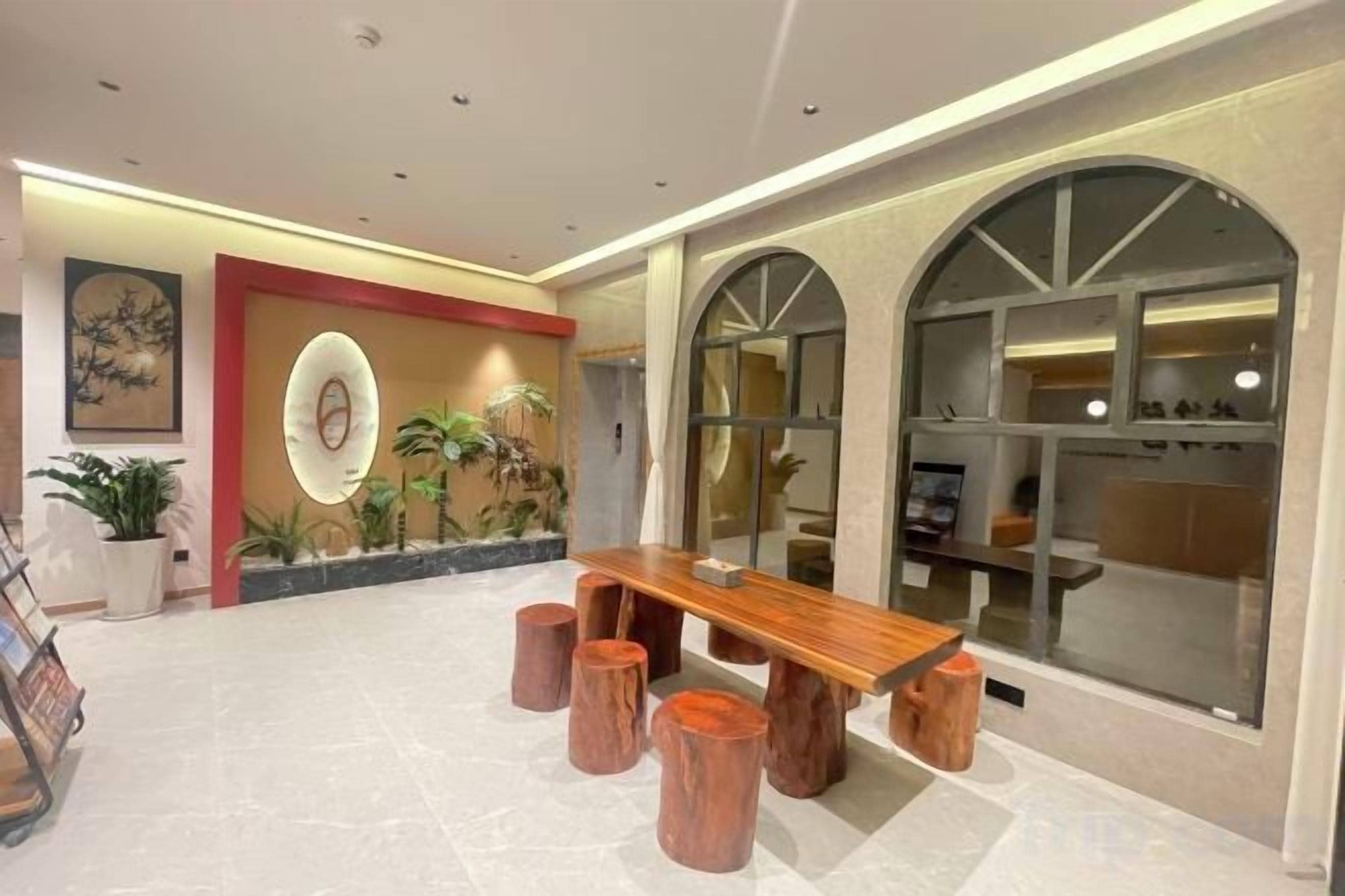 A spacious lobby with a wooden dining table, potted plants, and a large arched window.