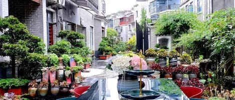 A narrow alley with a long table and chairs in the center, flanked by buildings with balconies and potted plants.