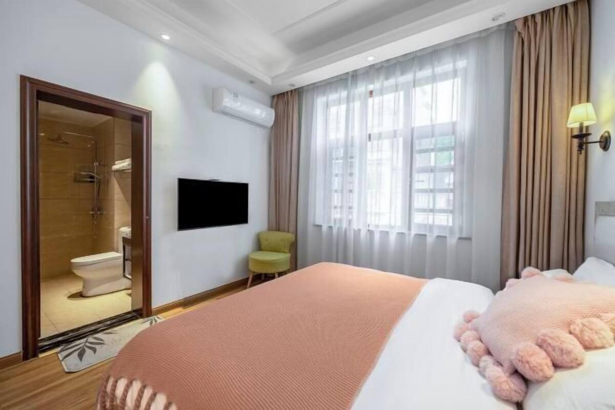 Ein Hotelzimmer mit Bett, Fernseher, einem Fenster mit Vorhängen sowie einem Badezimmer mit Dusche.