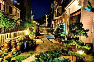 Una calle estrecha con macetas y mesas al aire libre, flanqueada por edificios.