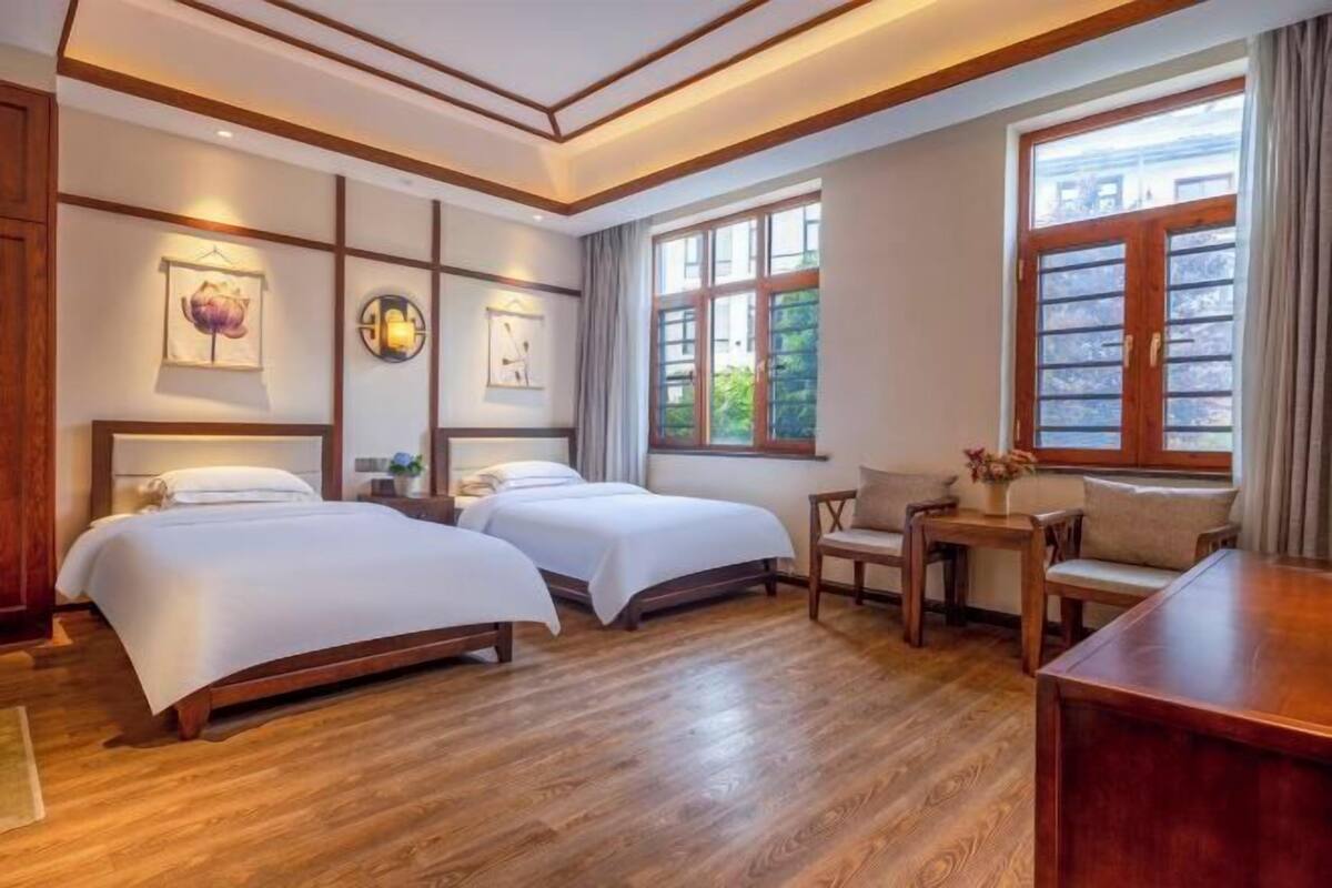 Ein Hotelzimmer mit zwei Betten, Holzboden, einem kleinen Tisch und einem Fenster mit Blick auf Grünflächen.