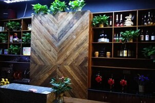 Una zona de bar con una pared de madera en diseño de tablero de ajedrez, estantes con botellas y plantas en macetas.