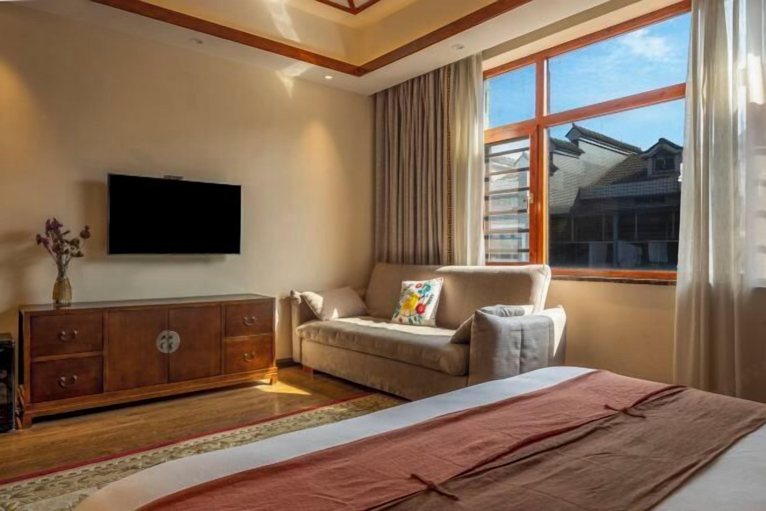 Un dormitorio con cama, sofá, televisor, ventana con cortinas y un armario de madera.