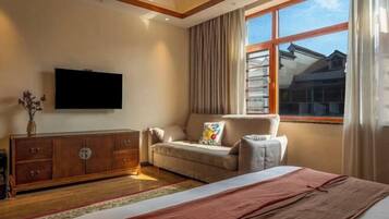 Un dormitorio con cama, sofá, televisor, ventana con cortinas y un armario de madera.