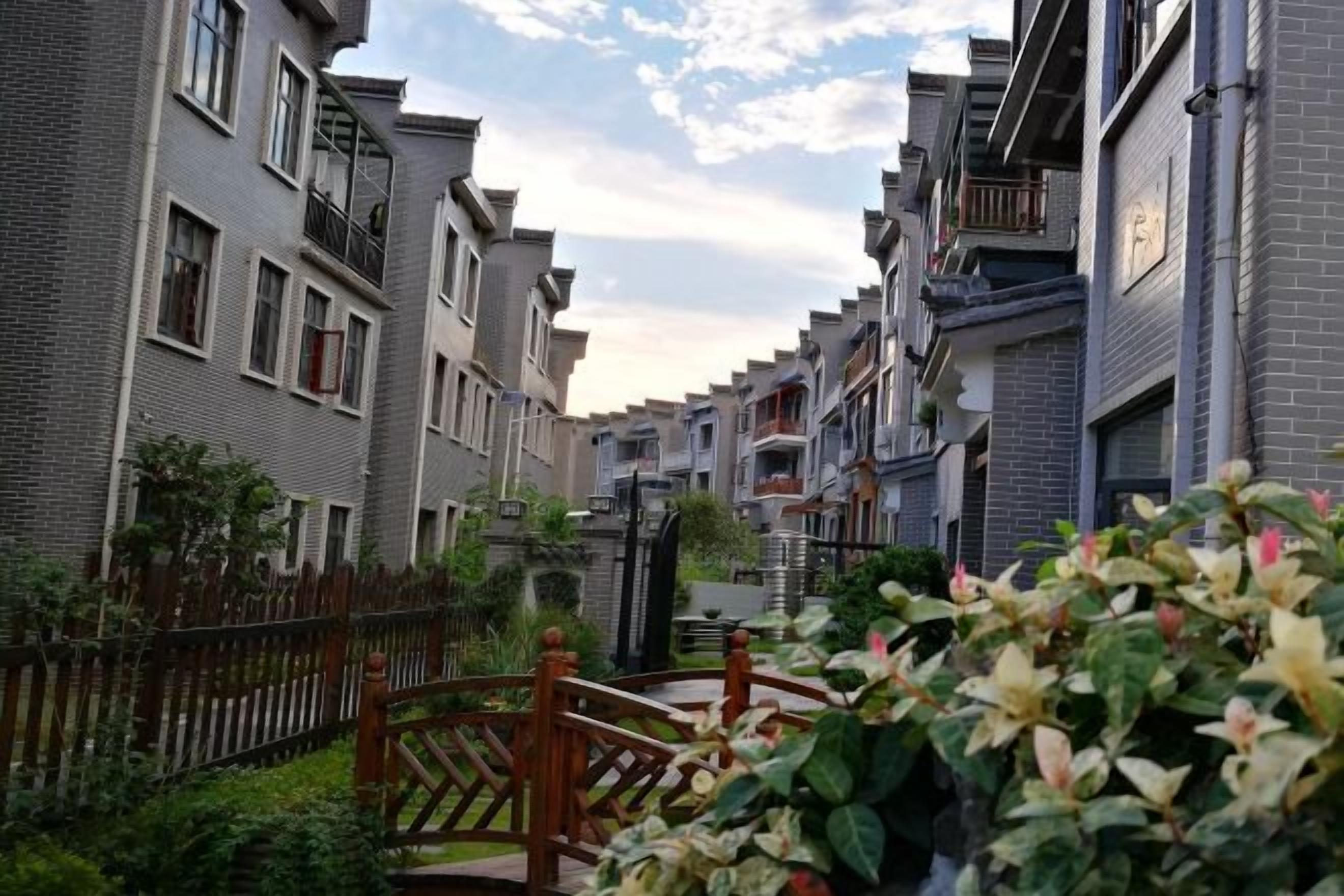 Una calle residencial con edificios de apartamentos modernos, una valla de madera y un pequeño puente.