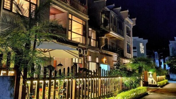 Un immeuble à plusieurs étages doté d’un balcon, d’un espace extérieur couvert aménagé en coin salon et d’une entrée bien éclairée.