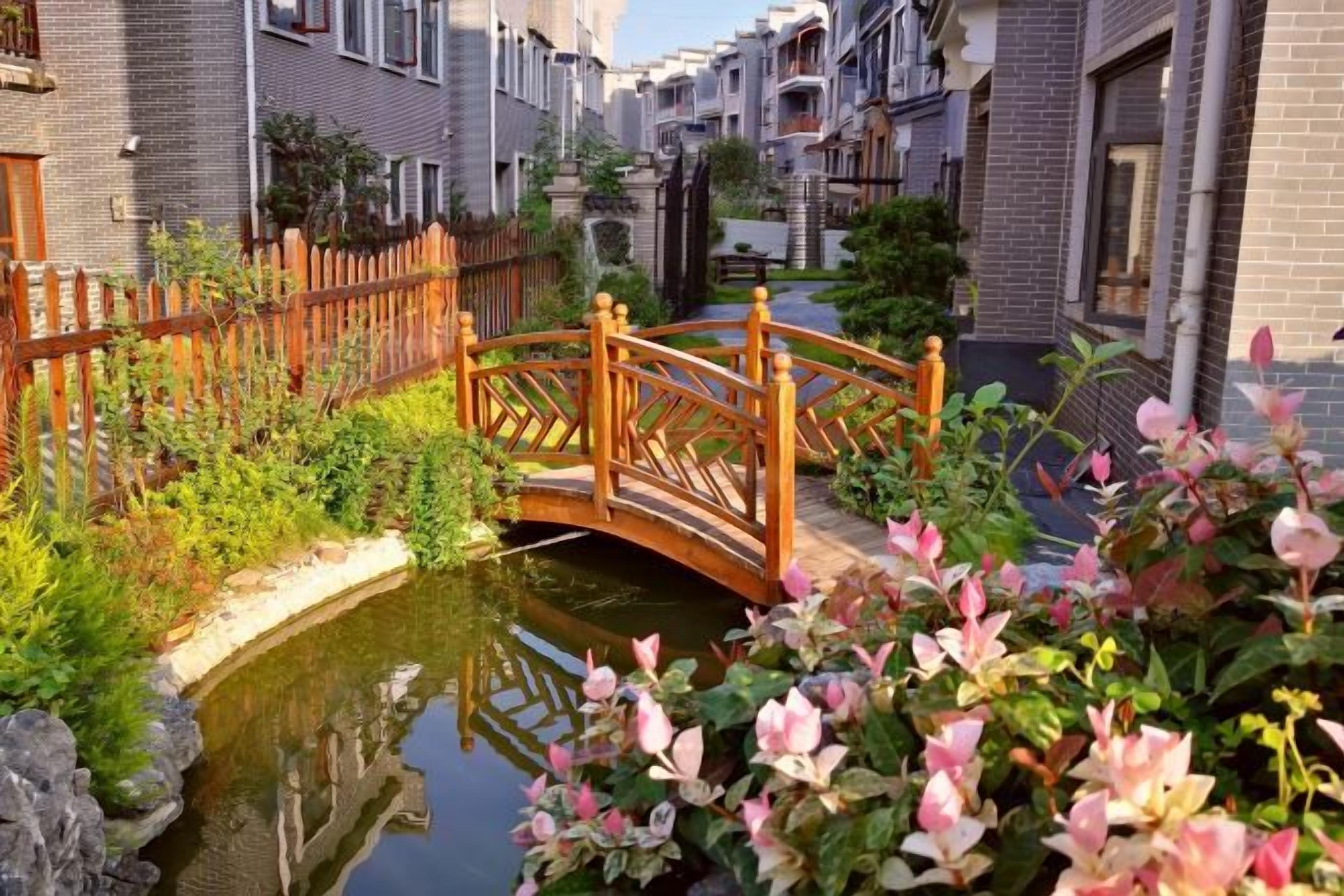Un canal estrecho con un puente de madera, rodeado de edificios de ladrillo y abundante vegetación.