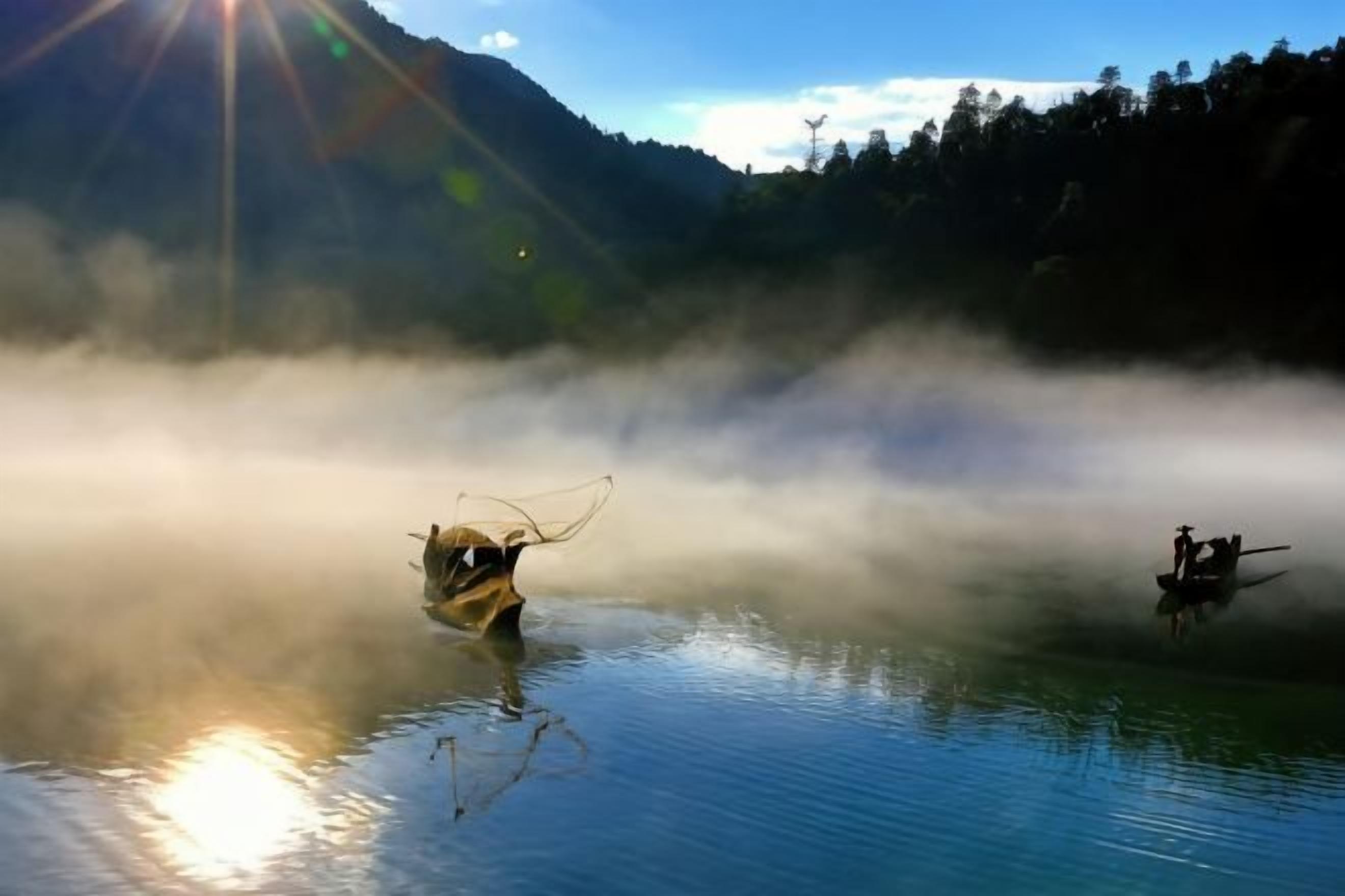 A calm lake with boats and mist, surrounded by forested hills.