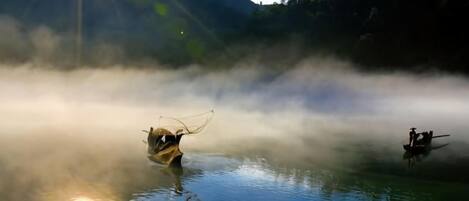 A calm lake with boats and mist, surrounded by forested hills.