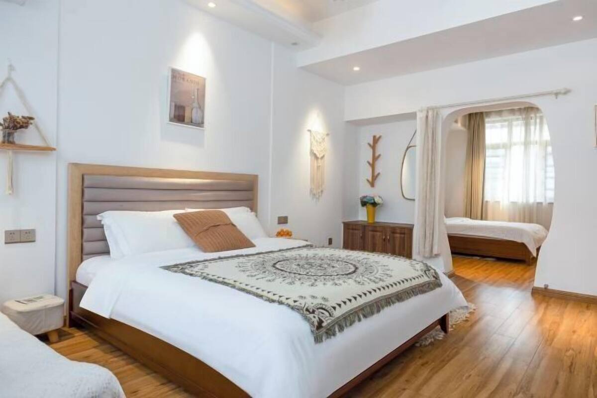 Ein Schlafzimmer mit einem großen Bett, einem Nachttisch, einem Fenster mit Vorhängen und einem an der Wand hängenden Kunstwerk.