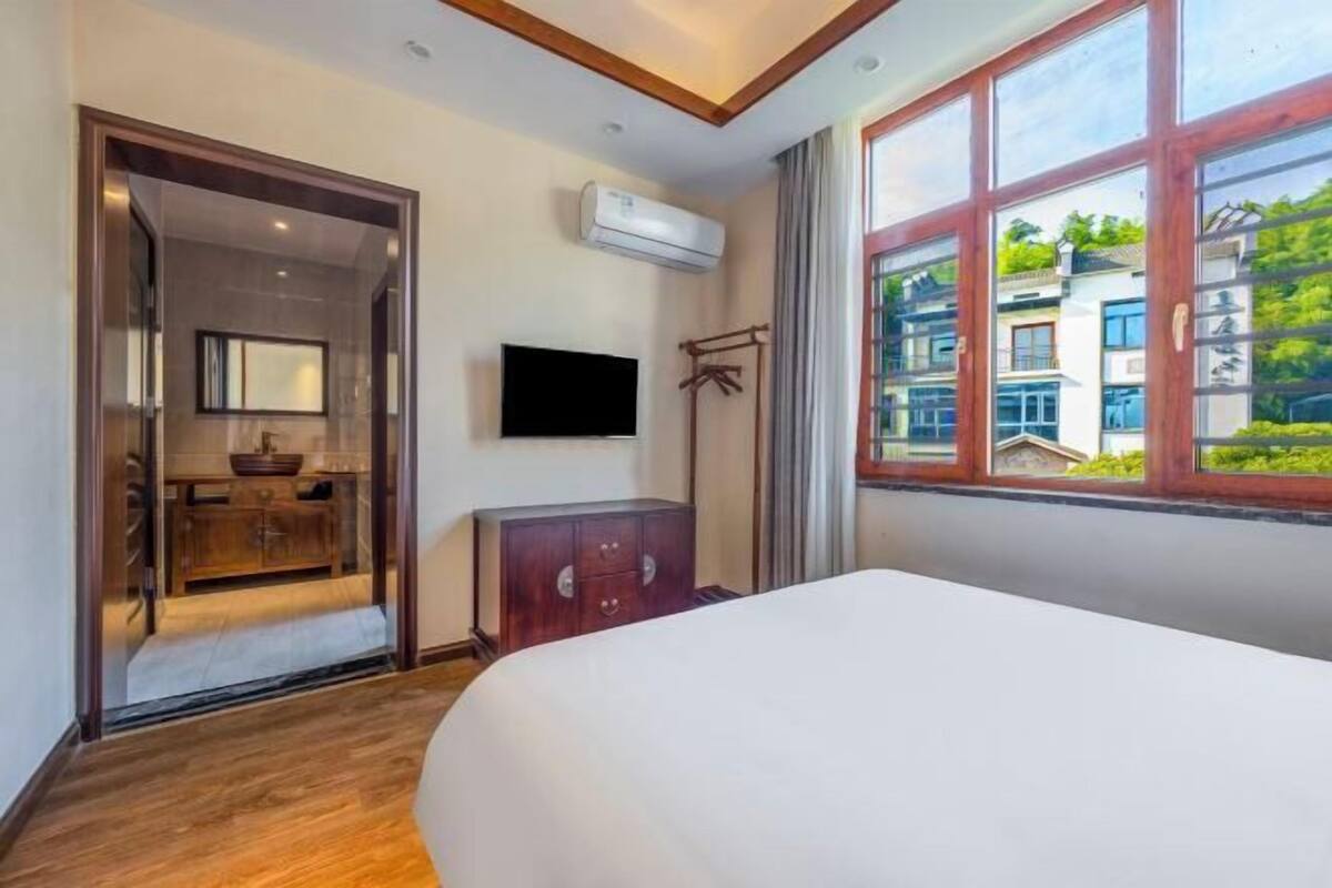 Ein Hotelzimmer mit Bett, Fernseher, Kleiderschrank und einem Fenster mit Blick auf Gebäude.