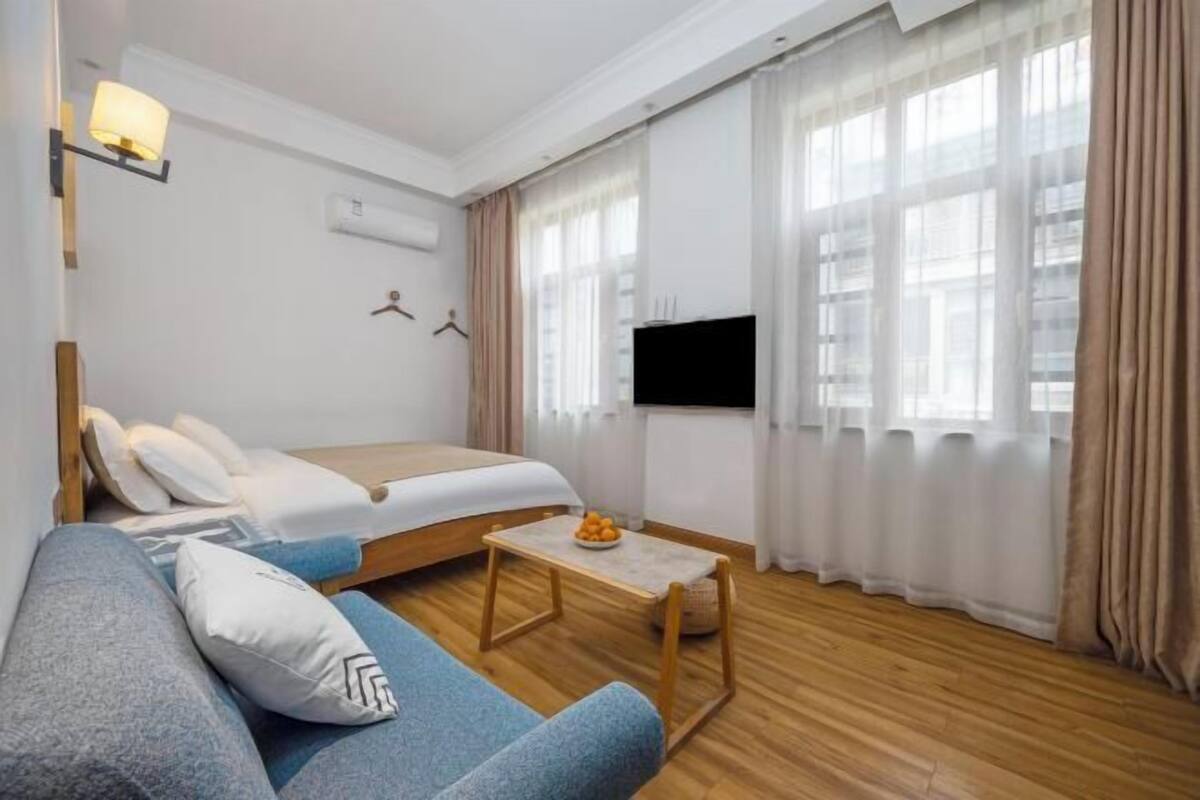Ein Hotelzimmer mit Bett, Sofa, einem kleinen Tisch, Fernseher und einem Fenster mit Vorhängen.