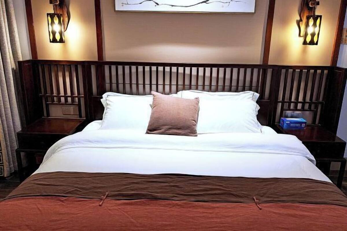 Ein ordentlich gemachtes Bett mit weißer und brauner Bettwäsche, an beiden Seiten mit Nachttischen und Lampen, in einem Zimmer mit Holzvertäfelung und einem an der Wand hängenden Kunstwerk.