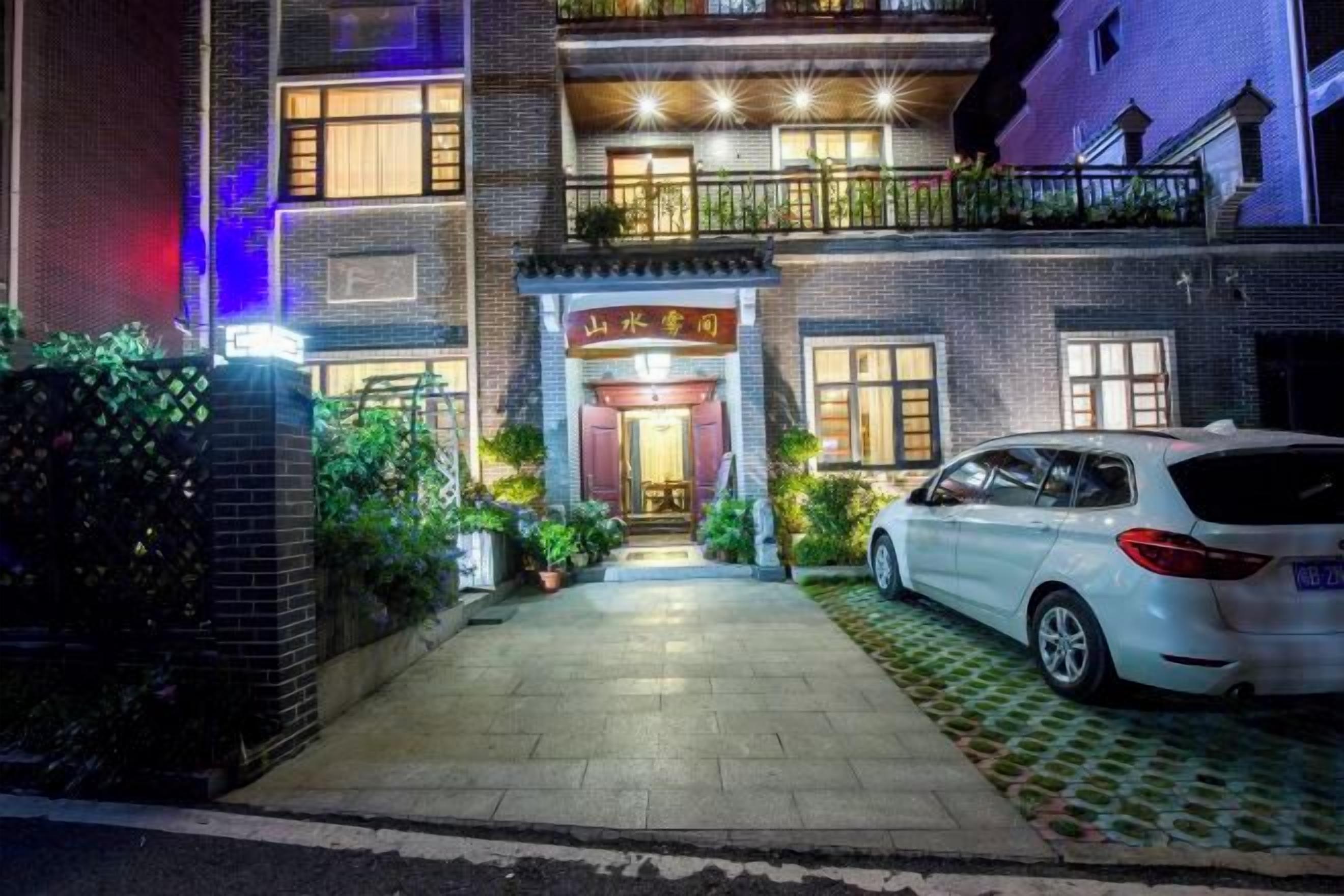 Un edificio de dos plantas con una puerta de entrada roja, un automóvil estacionado adelante y un balcón en el piso superior.