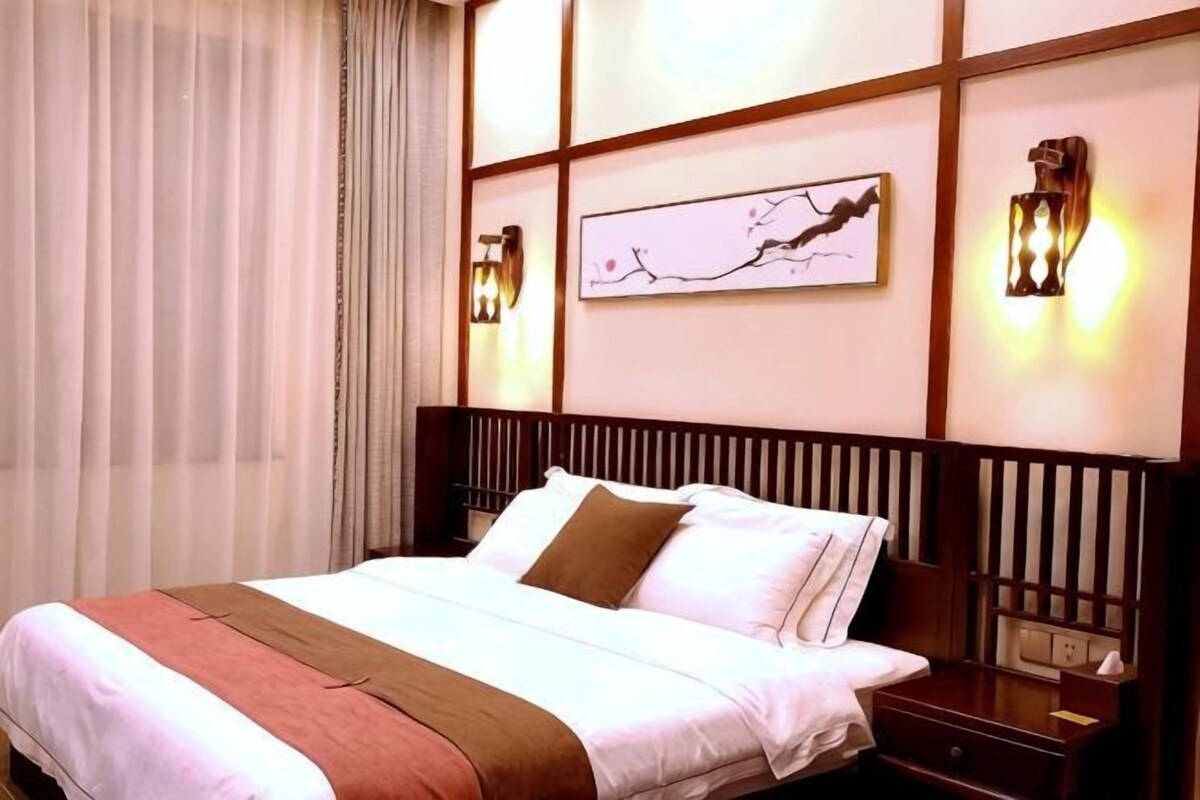 Una habitación de hotel con una cama grande, una mesita de noche, una lámpara de pared y una obra de arte enmarcada.