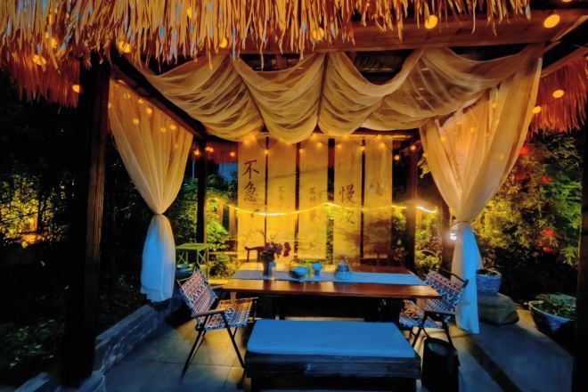 An outdoor dining area with a table and chairs, draped with fabric and string lights.