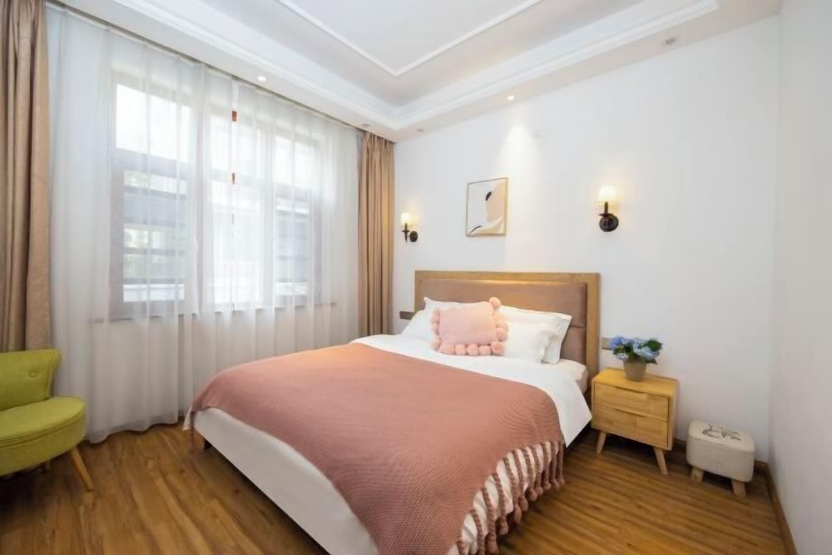 Una habitación de hotel con una cama, una mesita de noche, una silla y una ventana con cortinas.