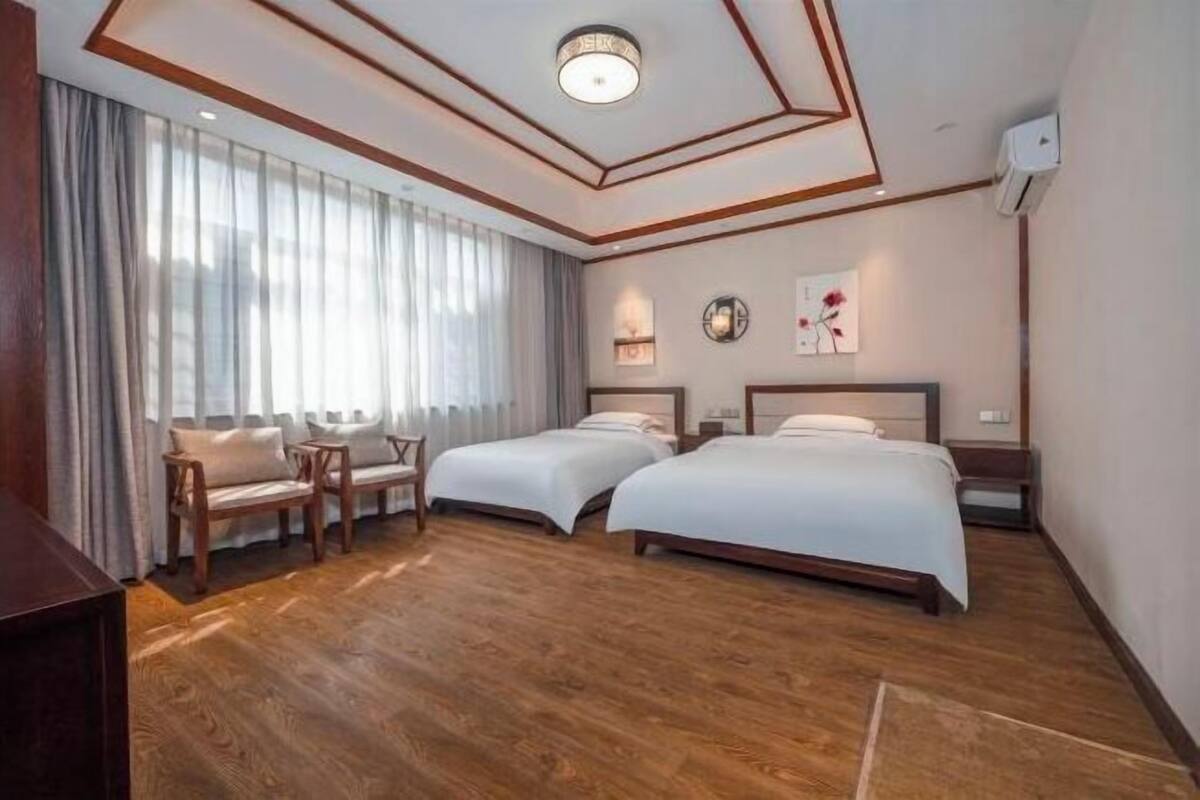 Ein Hotelzimmer mit zwei Betten, Holzboden, großem Fenster mit Vorhängen und Decke mit einer Einbauleuchte.