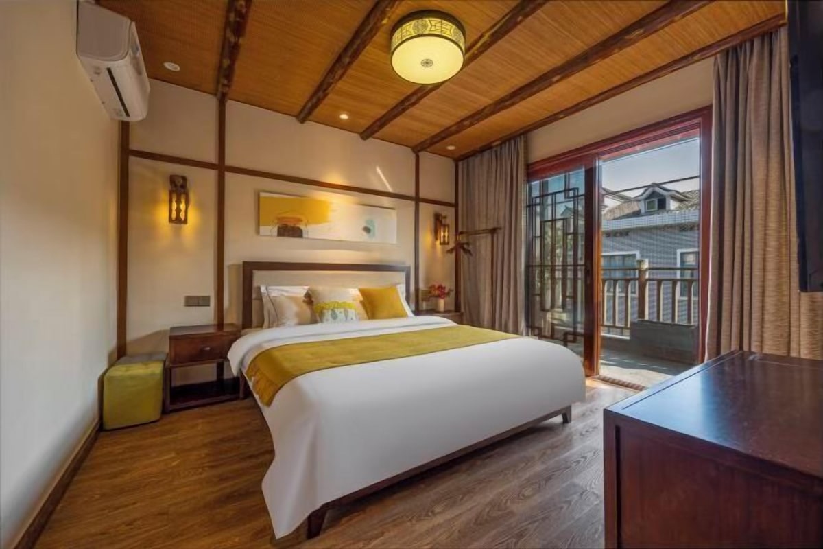 Habitación de hotel con cama, mesita de noche, lámpara y vistas a través de una puerta corrediza.