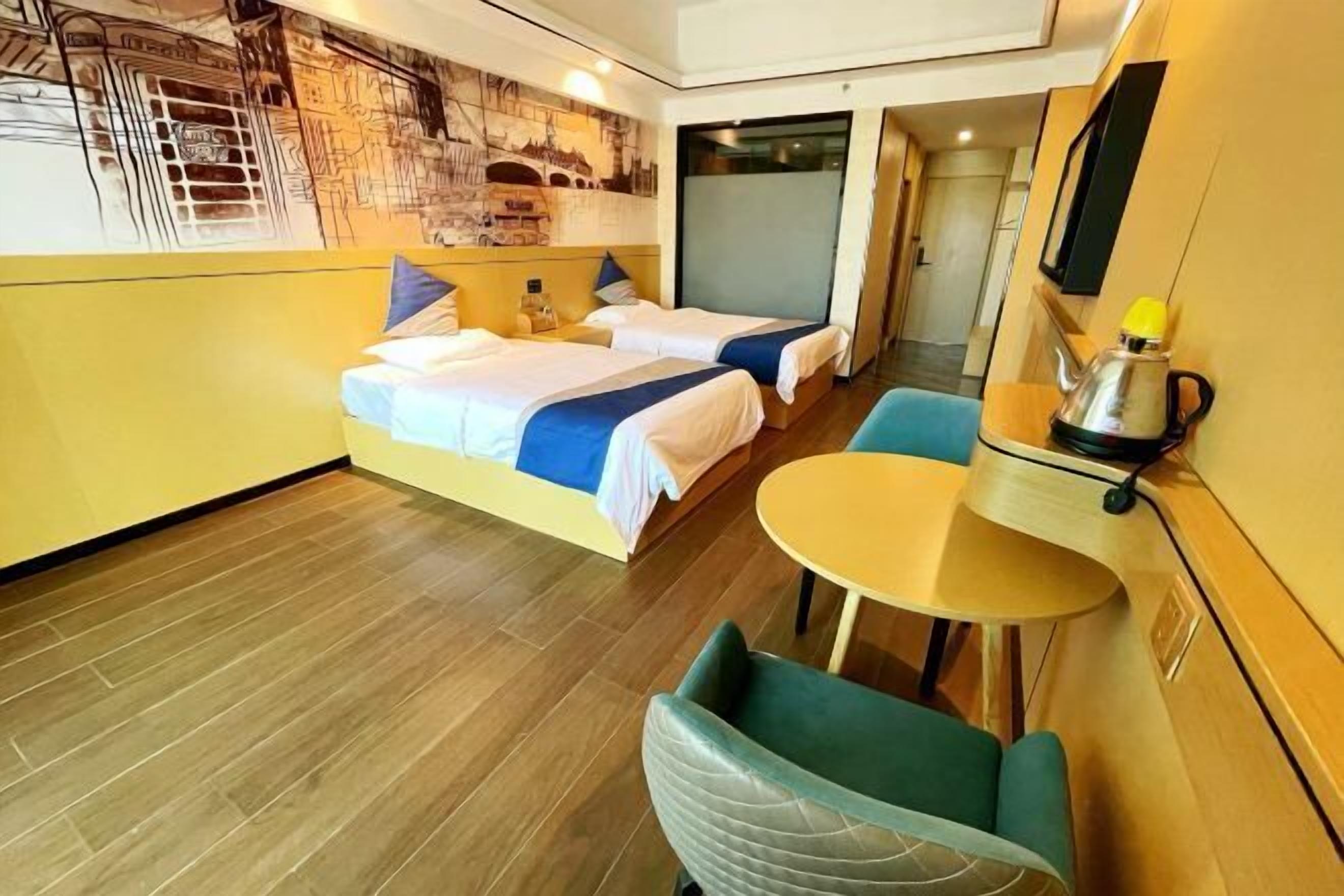 A hotel room with two beds, a small round table, and a green chair.