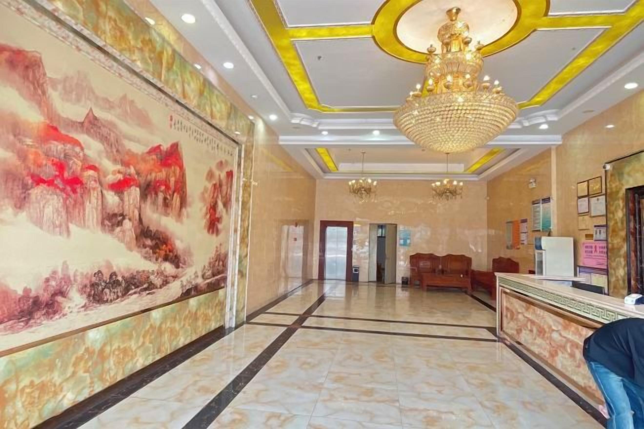 A hotel lobby with a reception desk, a large mural, and a chandelier.