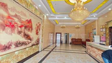 A hotel lobby with a reception desk, a large mural, and a chandelier.