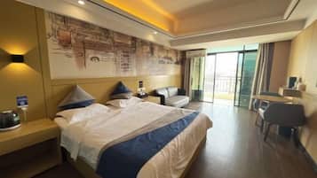 Una habitación de hotel moderna con una cama grande, una zona de estar con un sofá y sillones, una mesita pequeña y un ventanal con vistas a la ciudad.