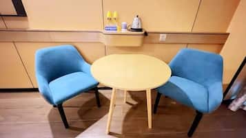 Una habitación con dos sillas azules alrededor de una mesita redonda, un estante con artículos de aseo y una tetera fijada a la pared.