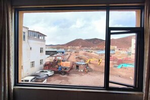 A window view of a construction site with a dirt ground, vehicles, and a crane. - Mangkang Chongqing Hotel (Markam)