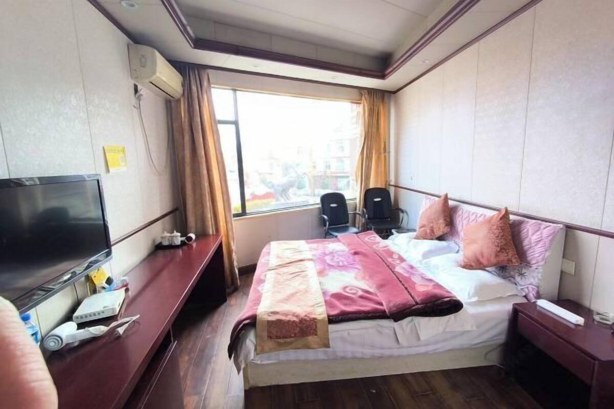A hotel room with a bed, a TV, a desk, and a window.