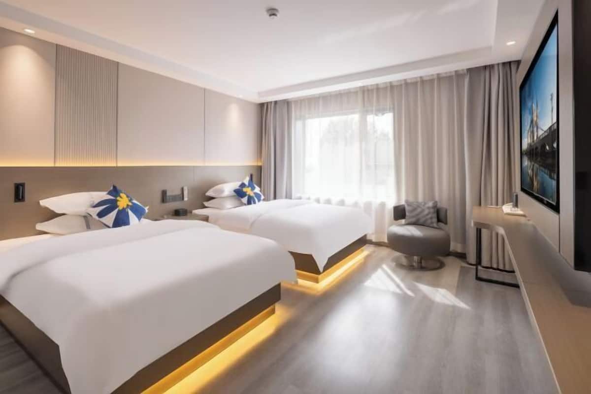 A modern hotel room with two beds, a seating area, and a large window with curtains.