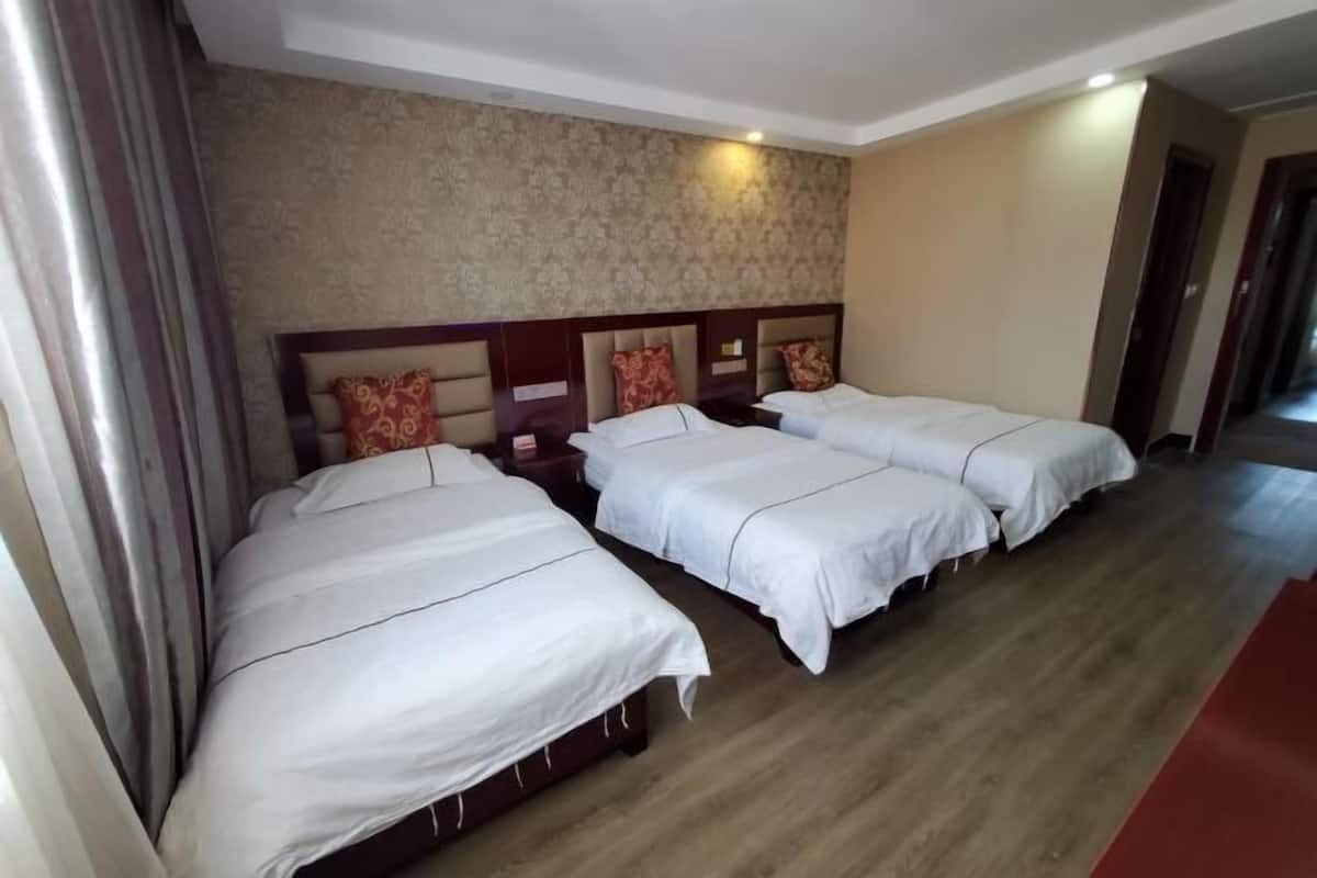 A hotel room with three single beds, wooden headboards, and a patterned wallpaper on the wall.