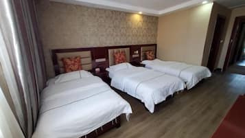 A hotel room with three single beds, wooden headboards, and a patterned wallpaper on the wall.