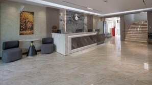 A modern reception area with a marble counter, grey upholstered seating, and a large abstract painting on the wall. - Yinhe Hotel (Burqin)