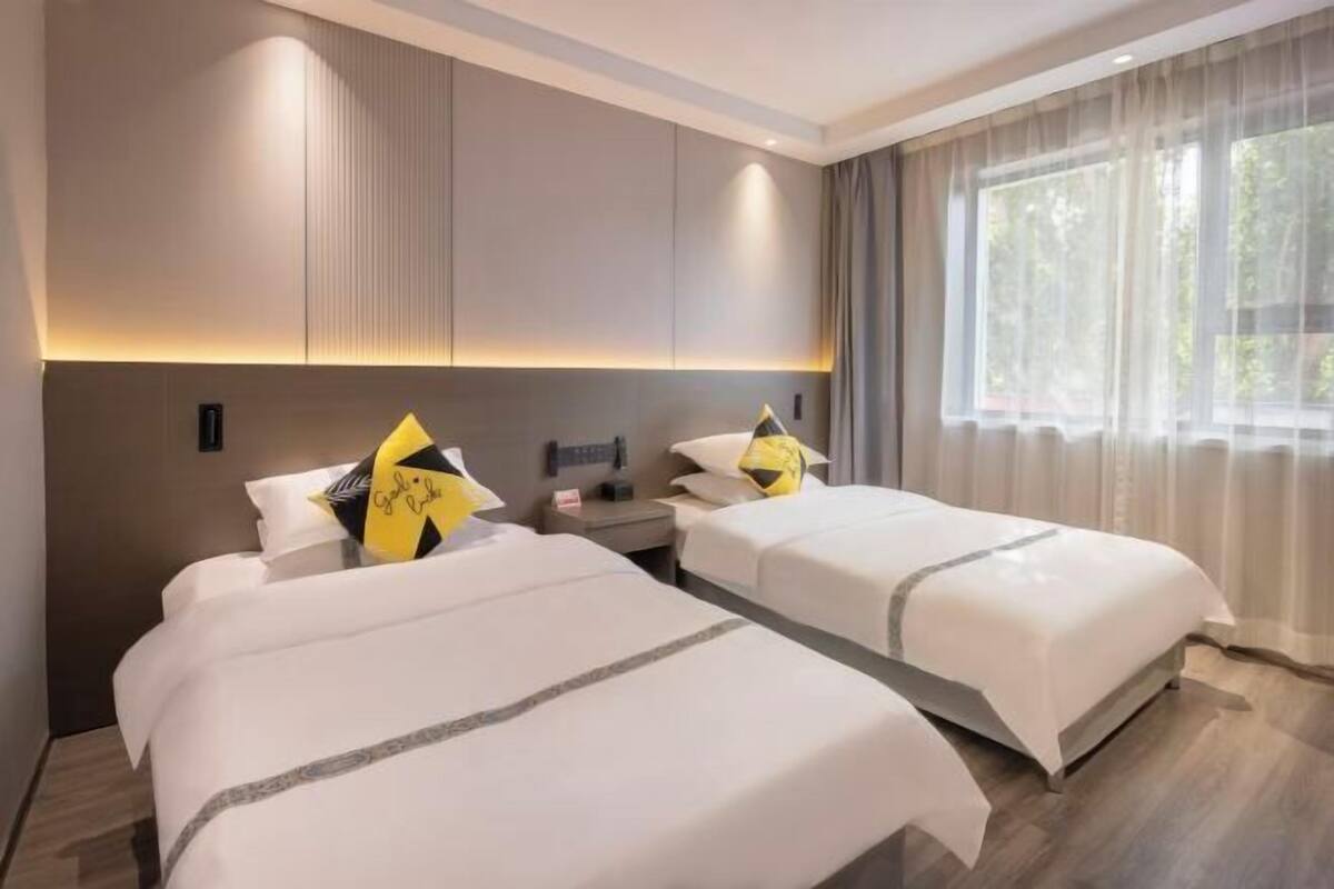 A hotel room with two beds, a bedside table, a nightstand, and a large window with curtains.