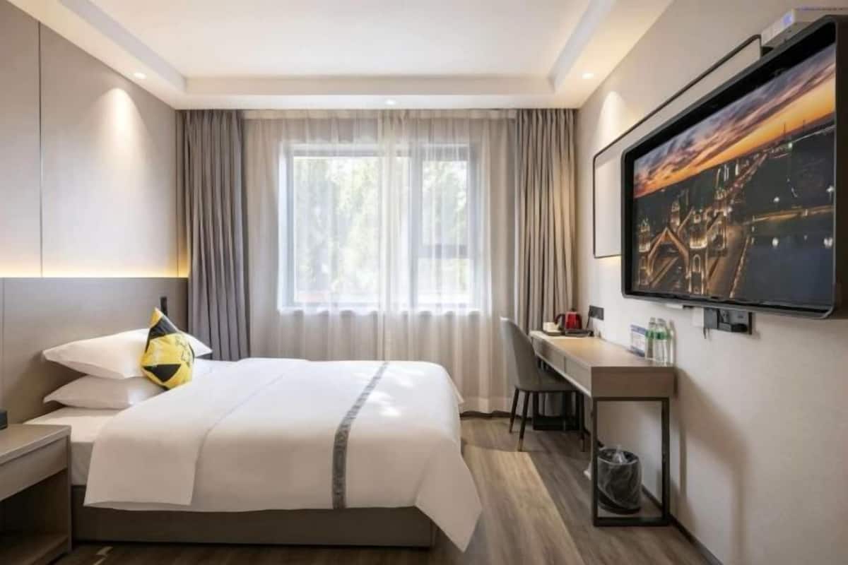 A hotel room with a bed, desk, and a large window with curtains.