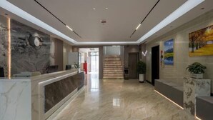 Un área de recepción moderna con suelo de mármol, un mostrador de recepción, una escalera y un cuadro en la pared.