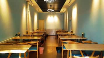 A long, narrow room with rows of wooden tables and chairs, a central aisle, and a ceiling with circular light fixtures.