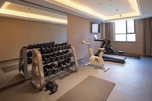A gym with exercise equipment, a treadmill, and a mirrored wall. - Yinhe Hotel (Burqin)